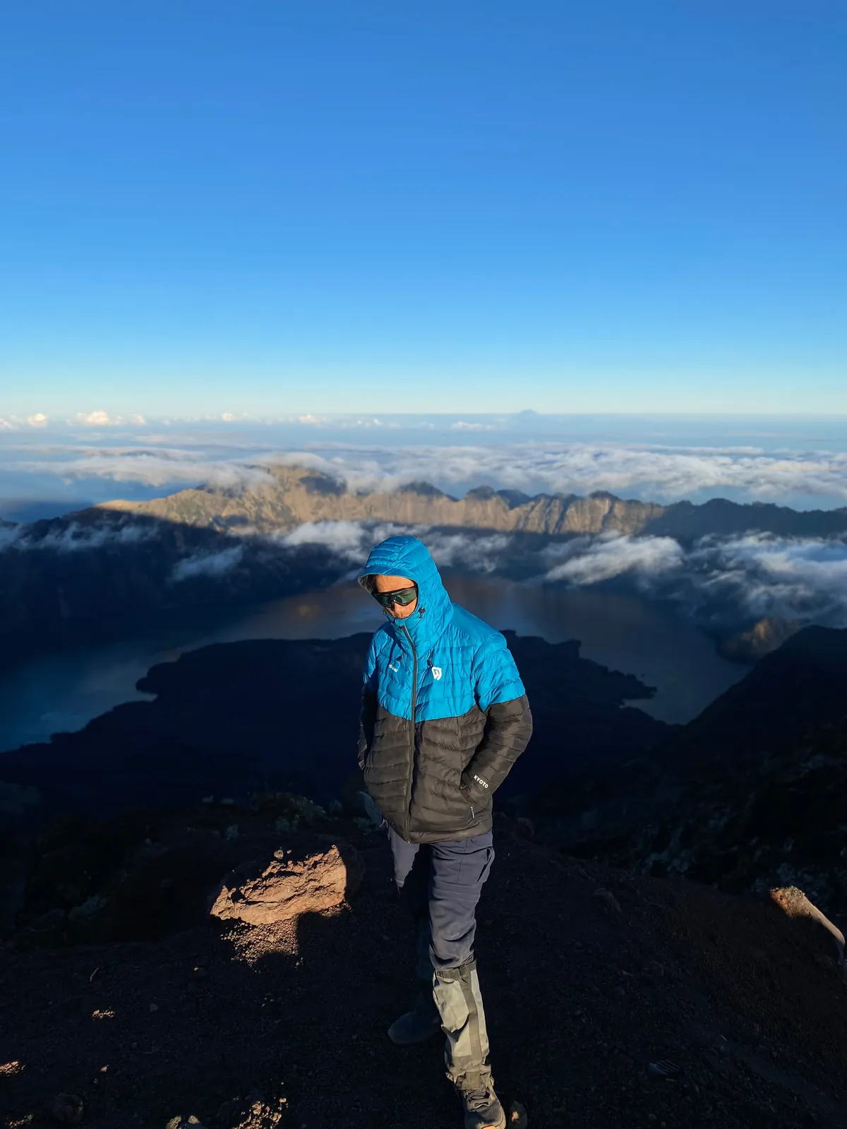 Trekker on the summit ridge of Mount Rinjani at sunrise, Segara Anak lake and the crater rim below the clouds
